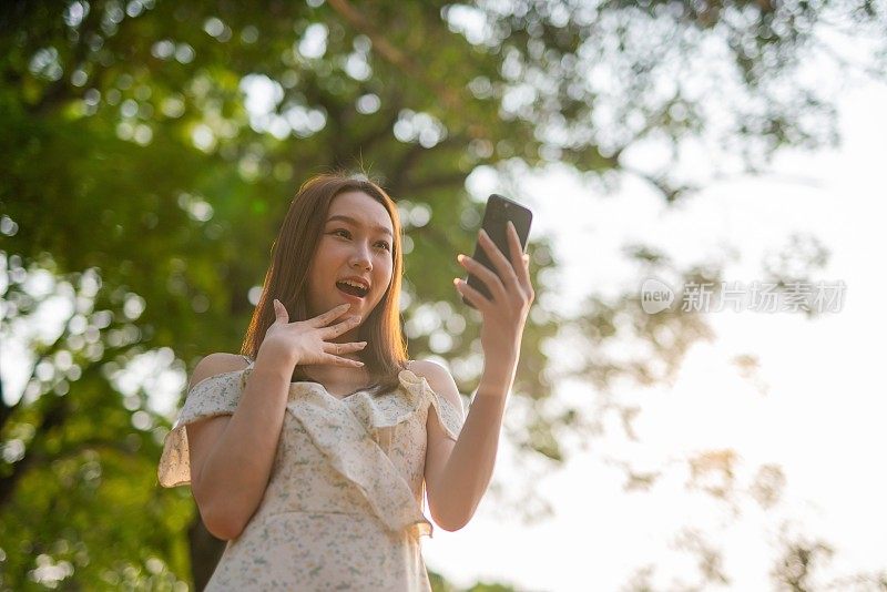 年轻的亚洲女子在公园里使用手机应用程序。美丽的女人在郁郁葱葱的绿色森林里查看手机上的应用程序