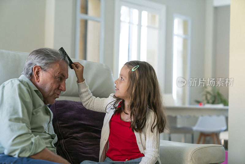 小女孩在家里的沙发上调皮地给爷爷梳头发