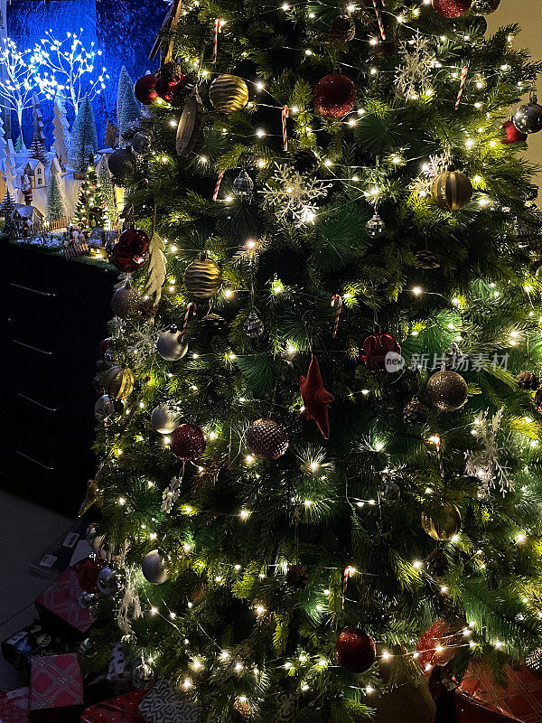 装饰物和装饰品的特写图像，包括银色的雪花，星形的小装饰品和人造圣诞树上的串仙女灯，圣诞村展示，重点在前景