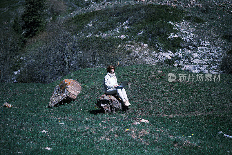 一位女士在山区自驾游时正在使用笔记本电脑