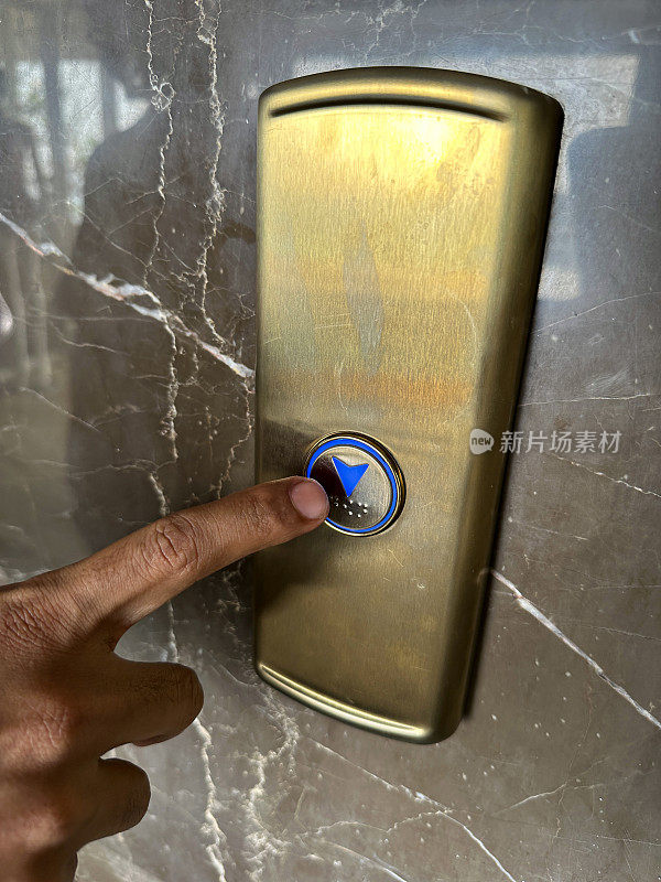 特写图像:无法辨认的人用食指按电梯呼叫按钮，电梯外高度抛光的大理石瓷砖墙，盲文，聚焦于前景