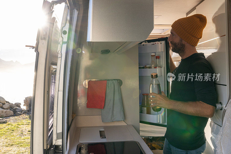 在货车里做饭的男人，海景。他打开冰箱