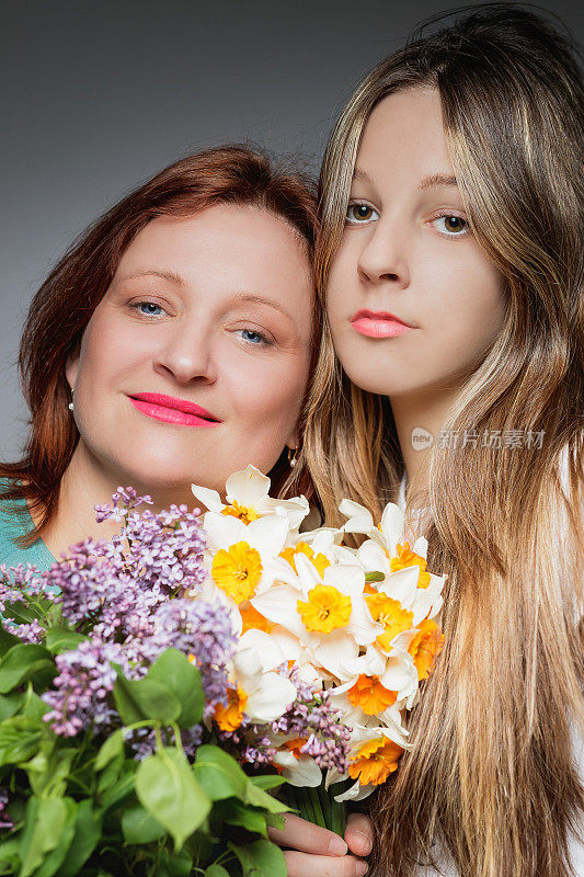 幸福的中年成年妇女站在她十几岁的女儿身边，两人都拿着花束