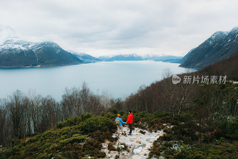 鸟瞰图:女人和男人带着狗呆在山顶上欣赏挪威冬季峡湾的风景