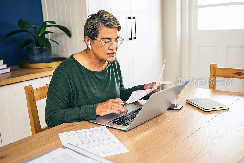 一个成熟的女人独自坐在家里，用她的笔记本电脑计算她的财务