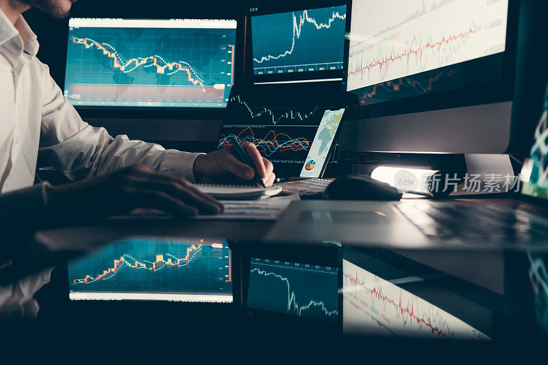 特写男性交易员分析股票市场数据，而坐在办公室工作站与多台电脑