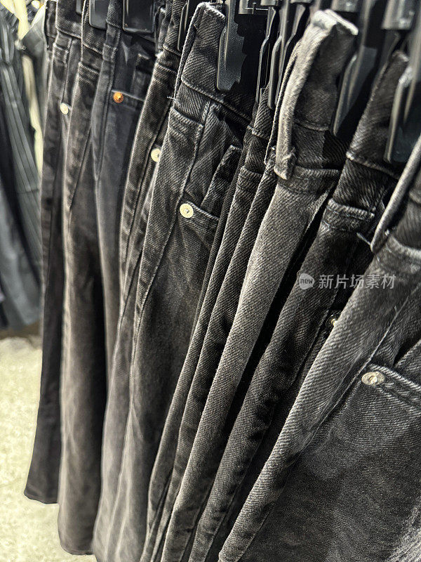 服装百货商店的特写图像，展示了一排女士黑色牛仔牛仔裤，裤子挂在塑料衣架上的衣架上，时尚的休闲服装，重点放在前景上