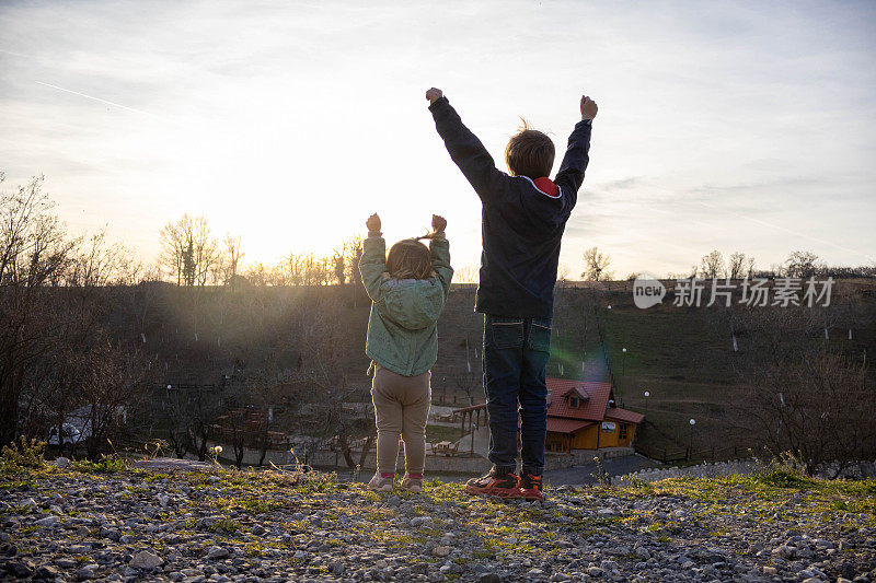 哥哥和妹妹背对着夕阳，举起了手臂