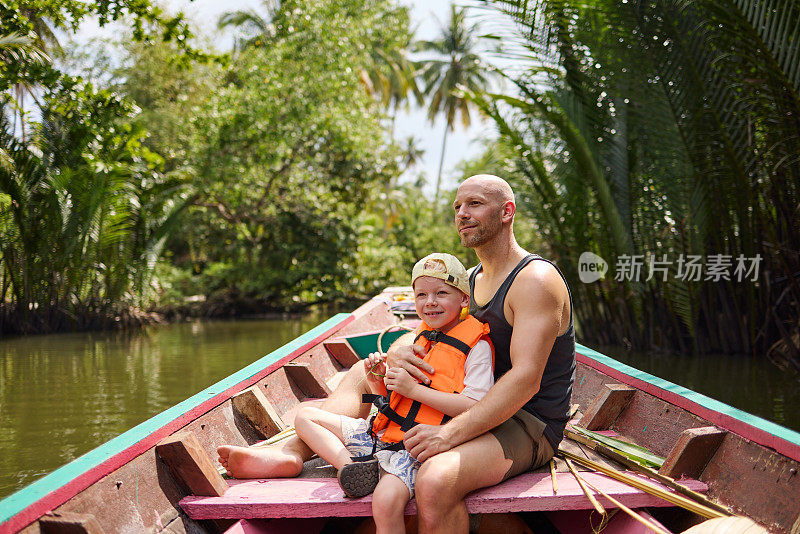 一位父亲和他的儿子坐在一艘长尾船上，在运河上旅行