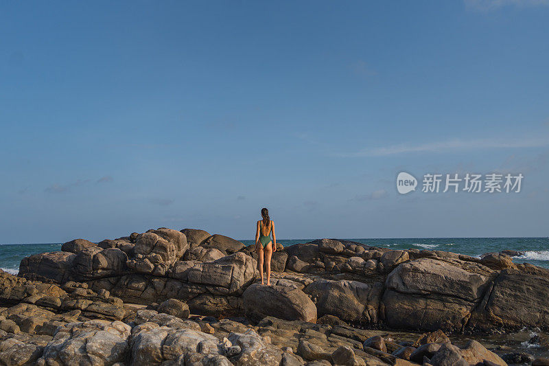 年轻女子在多岩石的海岸线上放松