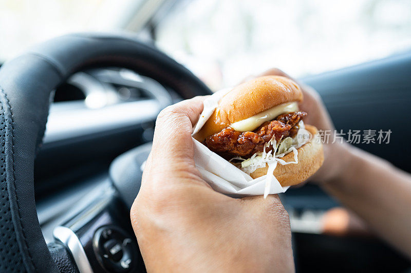 亚洲女士拿着汉堡在车里吃，危险而且有发生事故的危险。
