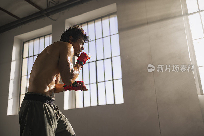 男运动员聚精会神地用红色拳击绷带包裹双手，准备在阳光普照的健身房里训练