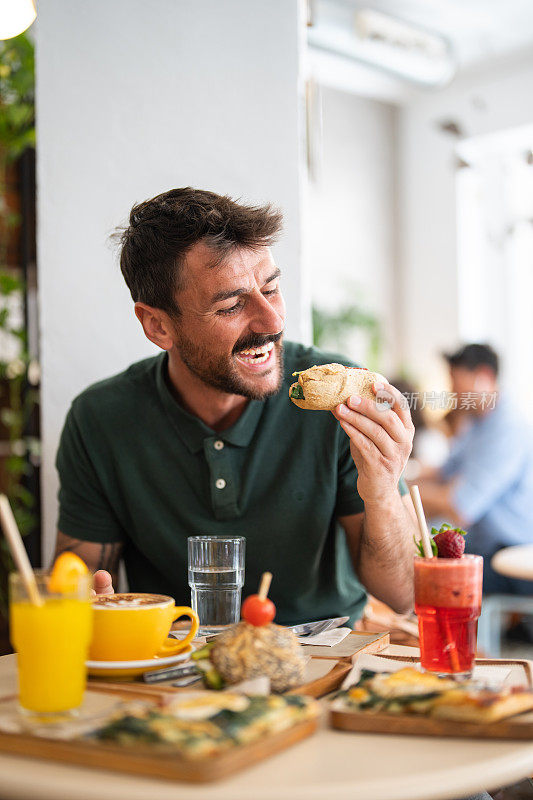 有胃口的白人胡子中年男人在吃三明治。