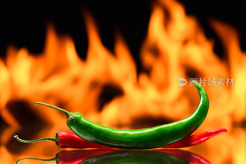 红色和绿色的辣椒，在燃烧的火的背景，火焰在黑色的背景，辛辣的香料