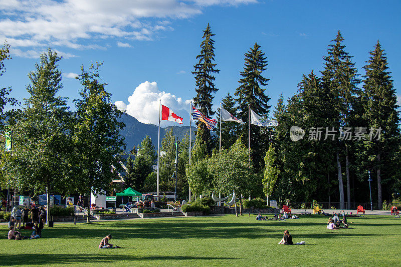 在惠斯勒村挥舞旗帜的杆子的观点。在一个阳光明媚的日子里，人们坐在绿色的草坪上