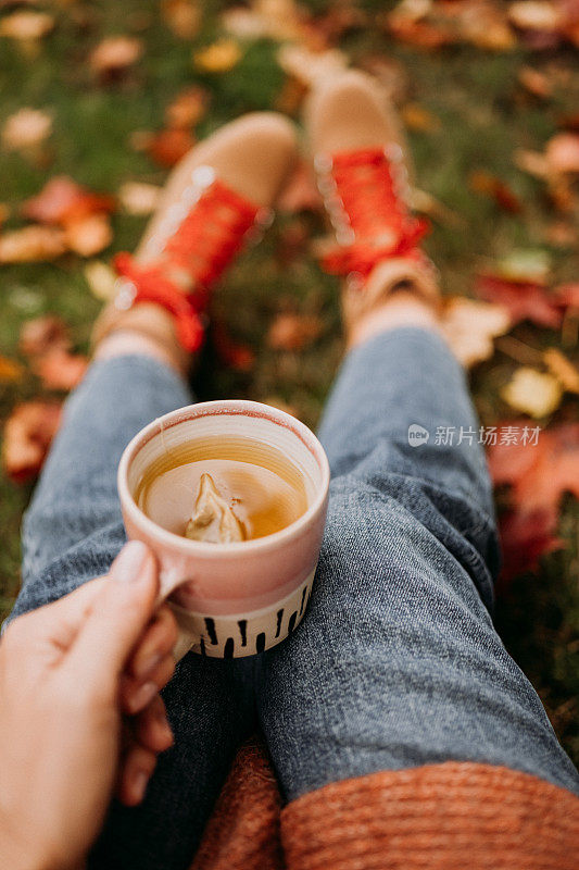在户外喝茶的女人在秋天休闲装近陶瓷茶杯