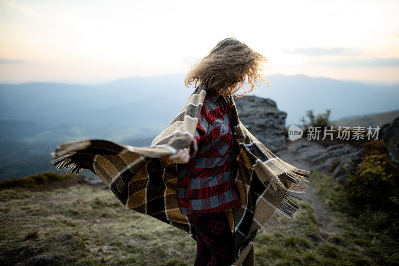 一个漂亮的年轻白种女人正披着花格毯子在秋日的群山中漫步。积极情绪