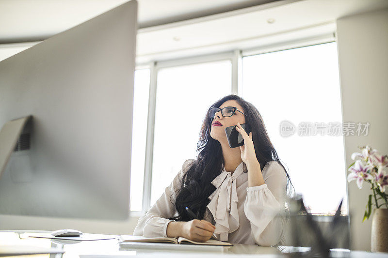 疲惫不堪的女人一边用着智能手机一边在办公室工作