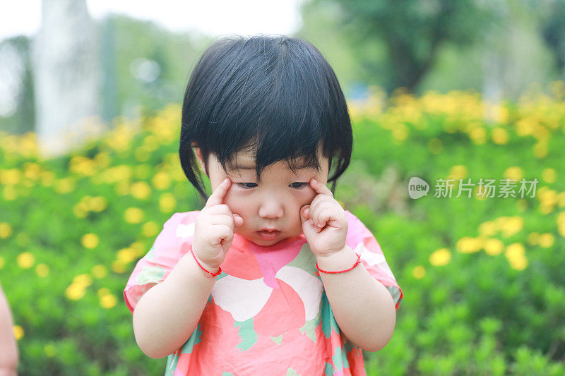 这是一个中国女婴的特写，她似乎在公园里思考，周围是黄花