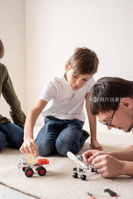 爸爸和孩子们坐在地毯上建造机器人车