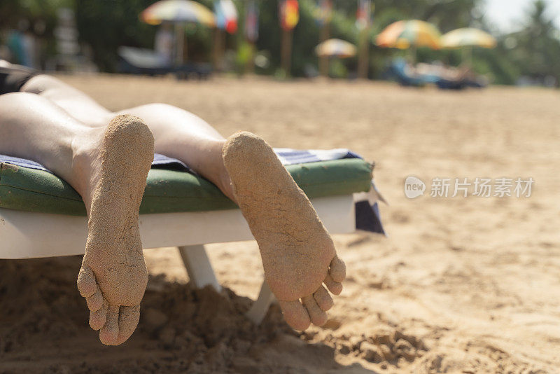 一个成熟女人的脚在热带海滩的躺椅上休息。