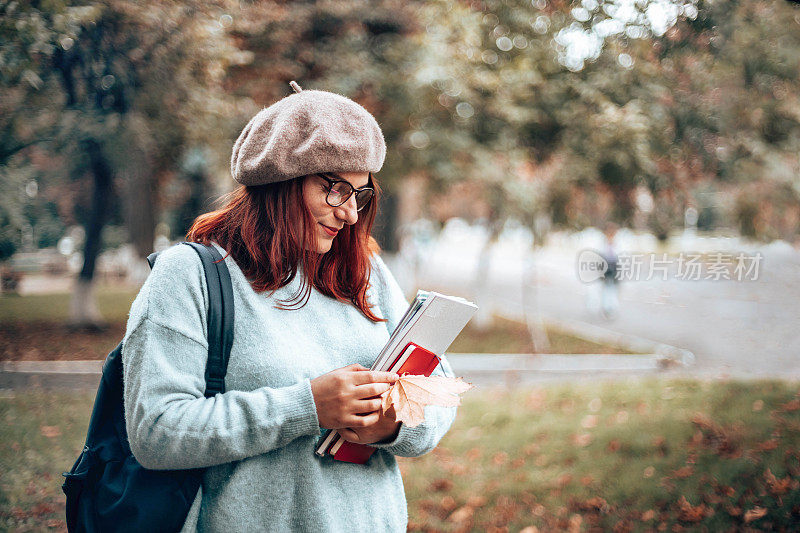 可爱的学生在公园散步，穿着休闲的衣服戴着眼镜，拿着笔记本和书籍在公园校园