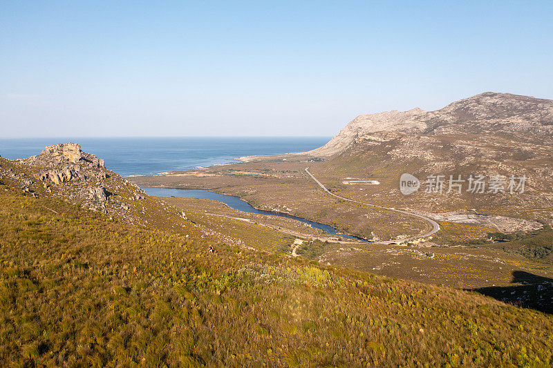 一个女人在山上沿着一条小路跑，俯瞰着大海