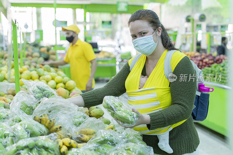 年轻的妇女抱着她的孩子在超市的水果和蔬菜选择他们的食物时看着相机的肖像