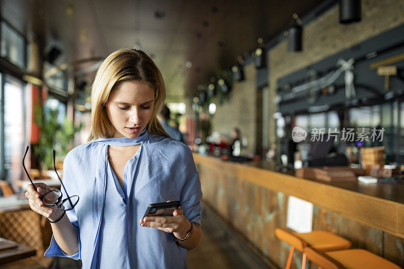 一位漂亮的金发女商人戴着眼镜正在使用她的手机Café。