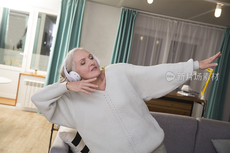 晚上，老妇人戴着耳机在家听音乐、唱歌、跳舞。老年人llifestyle。音频愈合。