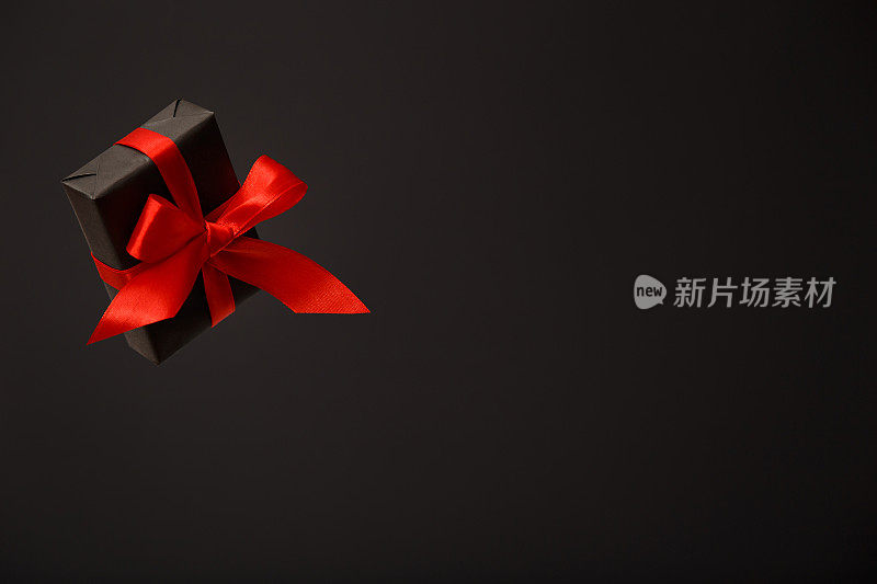 美丽的飞行黑色礼盒与红色蝴蝶结在黑色的背景。黑色星期五促销，圣诞节促销，折扣概念。情人节。父亲节