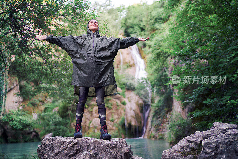 女人穿着雨衣，举起双手欣赏大自然