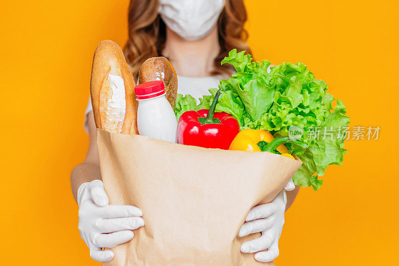 女性手里拿着一个纸袋，里面装着产品、蔬菜、草药，在橙色背景下隔离，隔离，冠状病毒，安全食品配送，呆在家里的概念