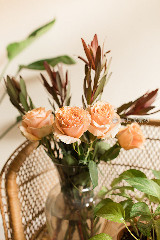软桃色乡村玫瑰与锈色秋叶插在波西米亚藤椅上的花瓶里