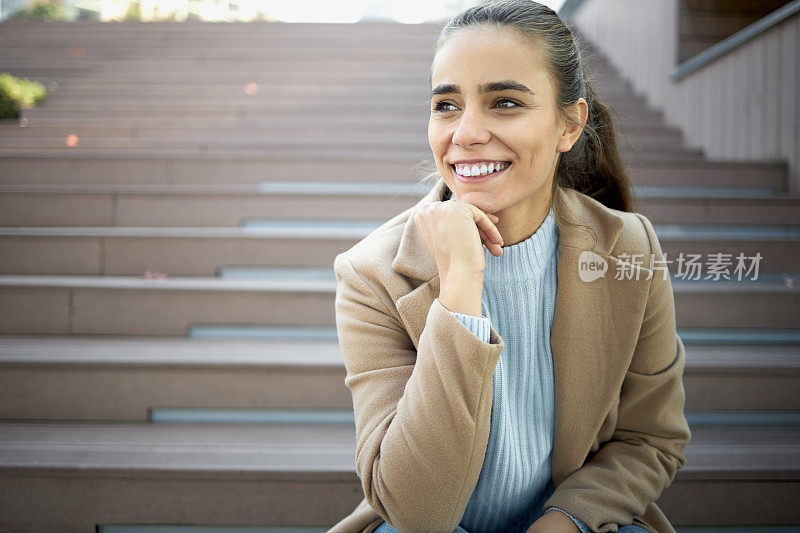 年轻微笑的女子坐在户外的长椅上，用着平板电脑，喝着咖啡，享受这一刻