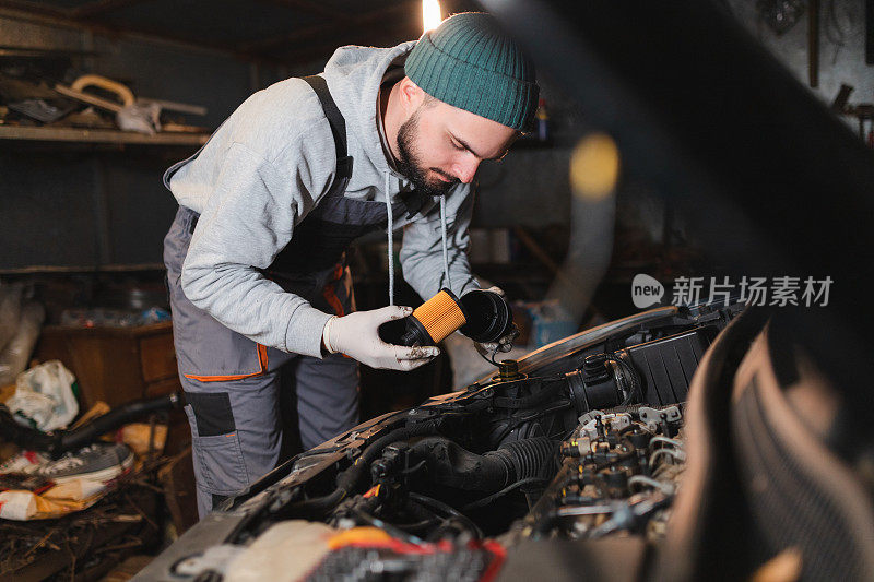 年轻的机械师正在他的车库里给一辆车更换机油和机油滤清器
