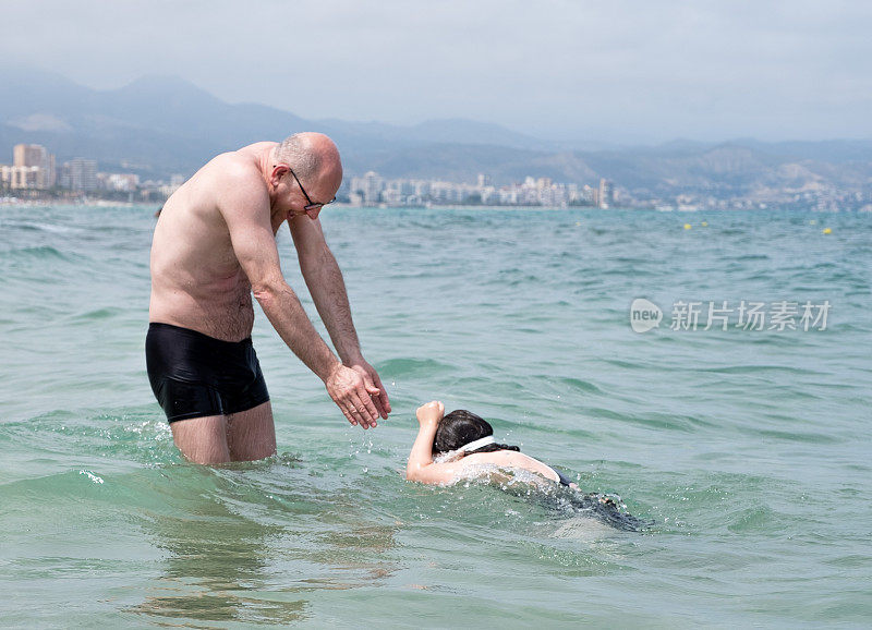 一个白人男子和一个孩子，一个7岁的女孩，在海里游泳和挣扎。