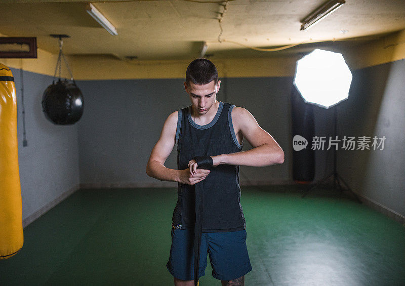 年轻强壮的男拳击手在拳击场上戴着拳击手套，在手上缠上保护绷带进行拳击训练。战士准备演习和训练