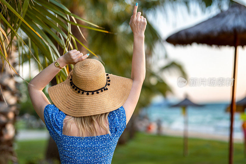 度假时沙滩上一个戴草帽的女人的后视图