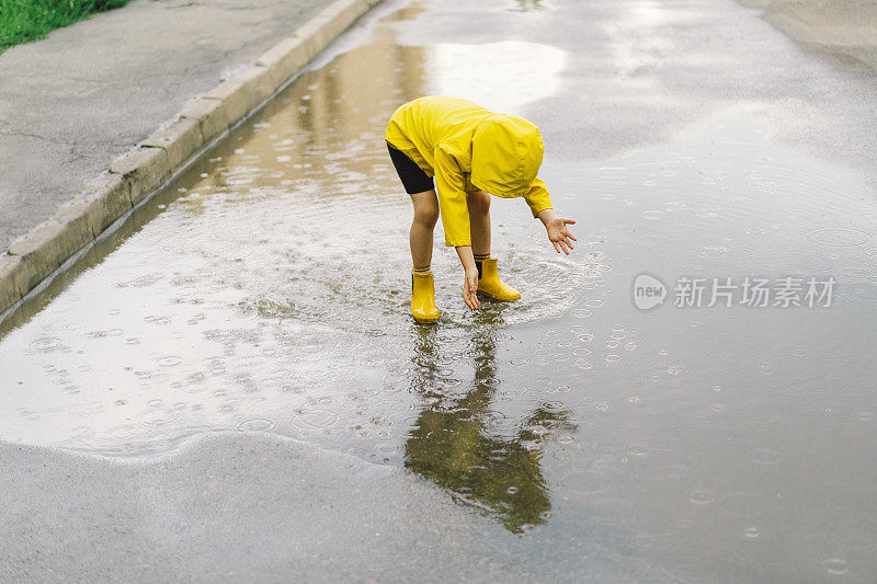 春天的一天，可爱的小男孩穿着雨衣和胶靴走过水坑