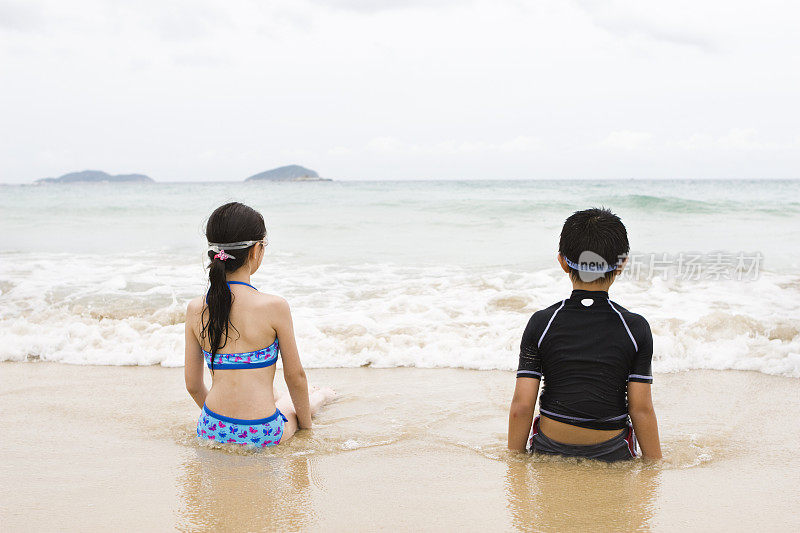 小男孩和小女孩坐在海滩上