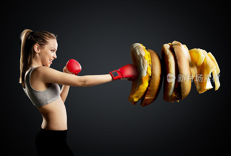 健康，年轻，精力充沛的女人拳击不健康的食物，黑色背景