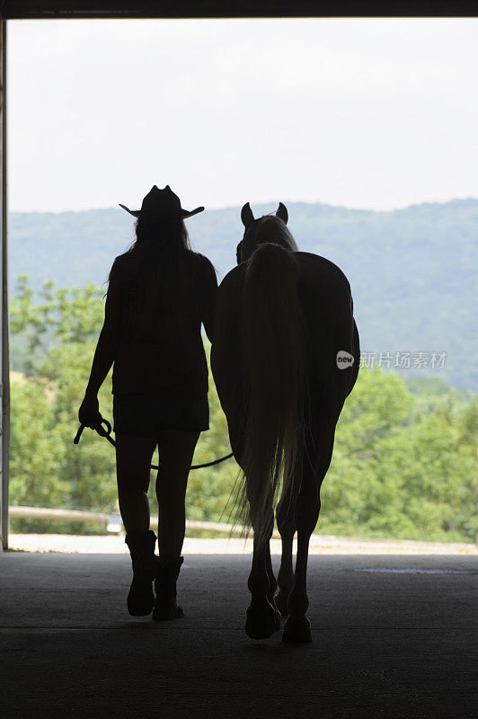 女人和马的剪影走在开放的夏天谷仓门