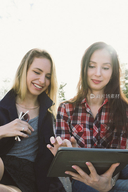 年轻漂亮的女人在公园里享受阳光，用平板电脑