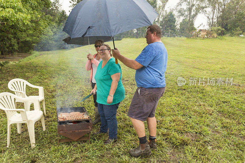 妇女遮阳伞做饭野营烧烤在雨中