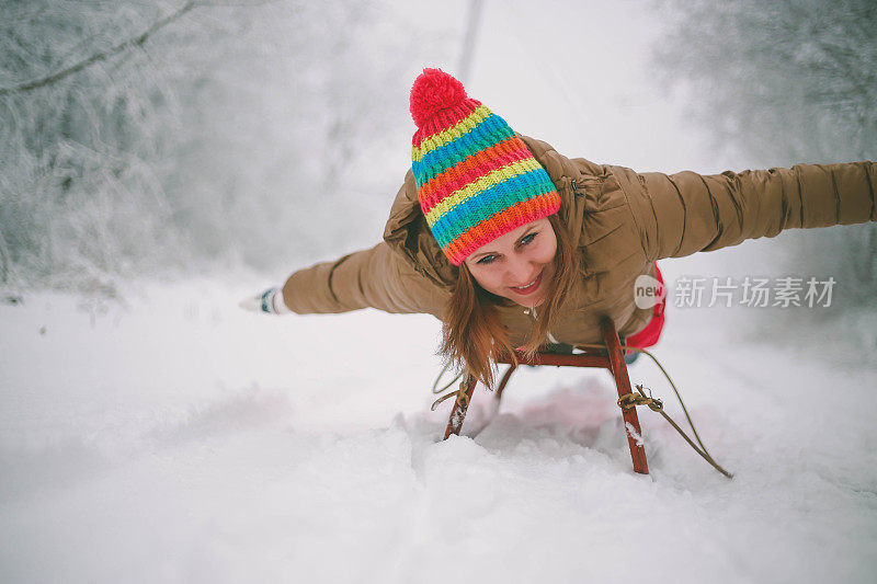 快乐的年轻女子在一个快速的雪橇骑下冰冷的斜坡