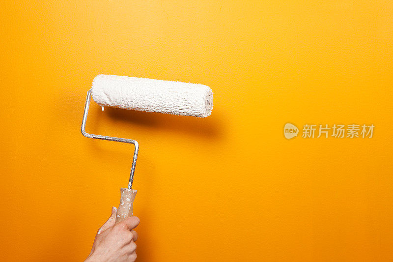 白色油漆滚轮对着橙色的墙