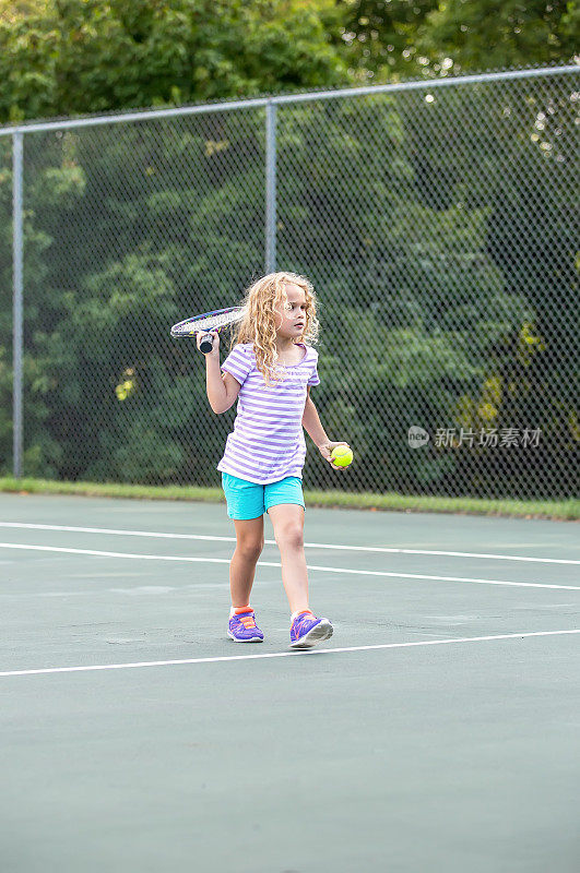 年轻的女孩在网球场上带着球拍和球