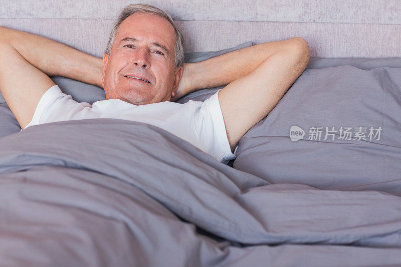 微笑的男人躺在床上，双手放在脑后