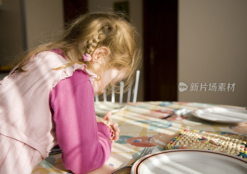 小女孩在饭桌上，在饭前做祷告